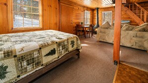 L'interno di una baita in legno con un letto, un divano, un tavolo da pranzo e un camino.