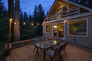 Une terrasse en bois avec une table et des chaises en verre, donnant sur une zone boisée.