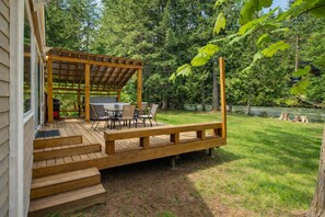 Une terrasse en bois avec mobilier d’extérieur, une pergola et une vue sur une rivière et une forêt.