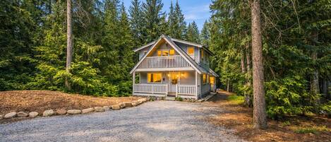 A two-story cabin with a porch, surrounded by dense forest.