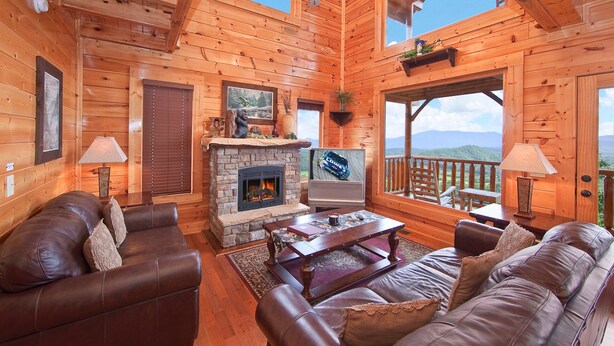L’intérieur d’un chalet en bois comprend une cheminée, des canapés en cuir, un téléviseur et un balcon offrant une vue sur les montagnes.