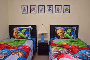 Quarto com duas camas, cada uma com um edredom com tema de super-herói. Há pôsteres de super-heróis emoldurados na parede acima das camas.