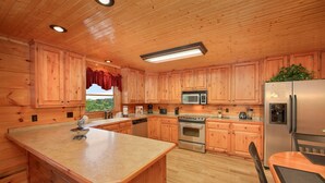 A wooden cabin-style kitchen with a central island, stainless steel appliances, and a window with a view.