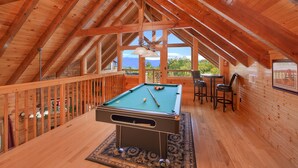 An attic room with a pool table, wooden deck, and a view of mountains.