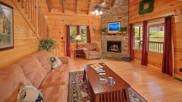 A cozy cabin interior with a wooden ceiling, a fireplace, a television, and a comfortable seating area.