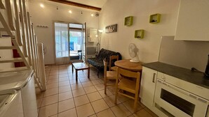 A compact kitchen with a dining area, a built-in oven, and a staircase leading to another room. - Cozy 2-Room House with Mezzanine, Pool & Parking - Saint-Cyprien Beach (Saint-Cyprien)
