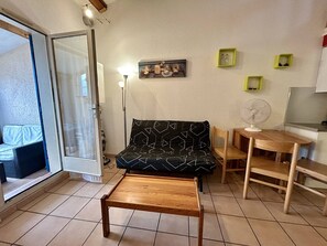 En hyggelig stue med en sofa, et træbord, en stol, et lille bord med en ventilator og en glasdør, der fører udendørs.