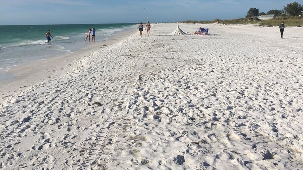 A sandy beach with footprints, a few people, and a tent in the distance. - Castaway Cottage + Beach + Heated Private Pool & Spa + GOLF CART INCLUDED! (Anna Maria)