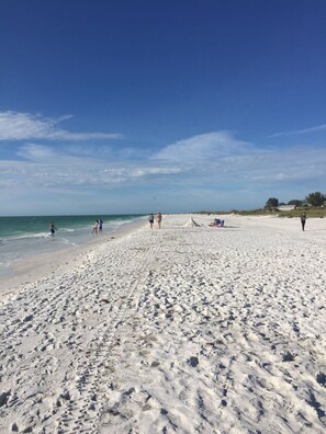 A sandy beach with footprints, a few people, and a tent in the distance.