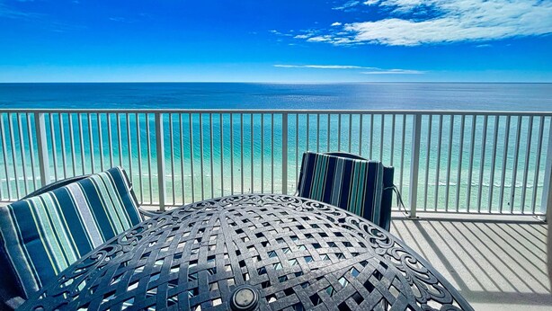 A balcony with a view of the ocean, a round metal table, and striped cushions. - Sit Back, Relax, and Enjoy the Beach in this Gulf-front Condo, Great Location (Panama City Beach)