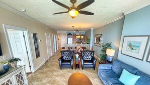 A spacious living room with a blue sofa, two leather armchairs, a wooden coffee table, and a ceiling fan. - Sit Back, Relax, and Enjoy the Beach in this Gulf-front Condo, Great Location (Panama City Beach)