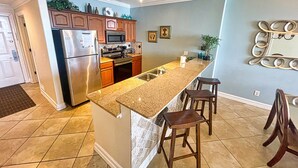 A kitchen with granite countertops, stainless steel appliances, wooden cabinets, and a bar area with stools. - Sit Back, Relax, and Enjoy the Beach in this Gulf-front Condo, Great Location (Panama City Beach)