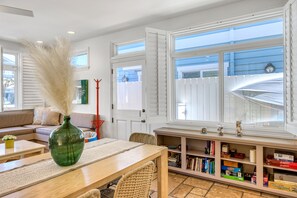 Uma sala de estar aconchegante com uma mesa de madeira, um vaso verde e uma estante repleta de livros e objetos decorativos.