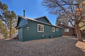 A two-story log cabin with a green exterior, a chimney, and a gravel driveway.