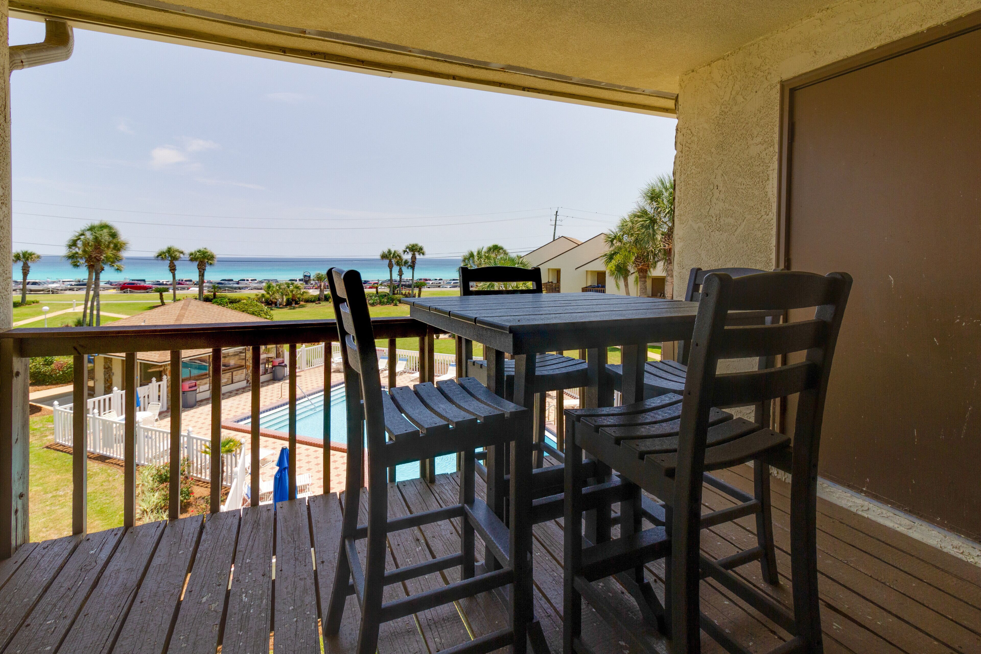 Eine Holzterrasse mit Tisch und Stühlen, mit Blick auf ein Schwimmbecken und einen Strand.