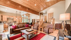 A spacious living area with a wooden ceiling, a fireplace, a staircase, and a kitchen with wooden cabinets.
