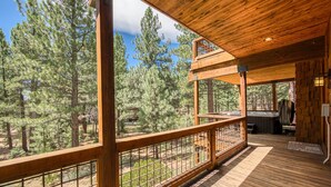 A wooden deck with a view of a forest, a hot tub, and a stone wall.