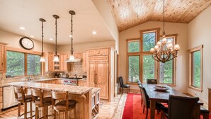 A spacious kitchen with wooden cabinets, a large island with bar stools, and a dining area with a red rug.