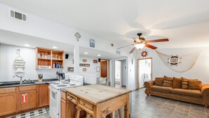 Una cocina moderna con armarios de madera, una estufa y una mesa de comedor. Hay un ventilador de techo y un sofá en la sala de estar.