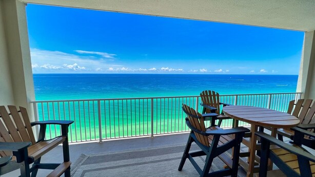 A balcony with a view of the ocean, wooden chairs, and a table. - 4 Bedroom Platinum Designer End Unit Incredible Gulf Views! Free Beach Chairs (Panama City Beach)