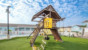 A playground with a wooden climbing structure and a swing set. - Spacious coastal cottage at Pirates Bay! Just a short drive to the beach and one (Port Aransas)
