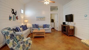 A living room with a white sofa, a patterned armchair, a wooden coffee table, and a ceiling fan. - Spacious coastal cottage at Pirates Bay! Just a short drive to the beach and one (Port Aransas)