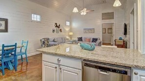 A kitchen with a granite countertop, white cabinetry, a dishwasher, and a ceiling fan. - Spacious coastal cottage at Pirates Bay! Just a short drive to the beach and one (Port Aransas)