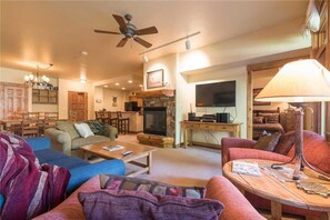 A cozy living room with a fireplace, a television, and a ceiling fan.
