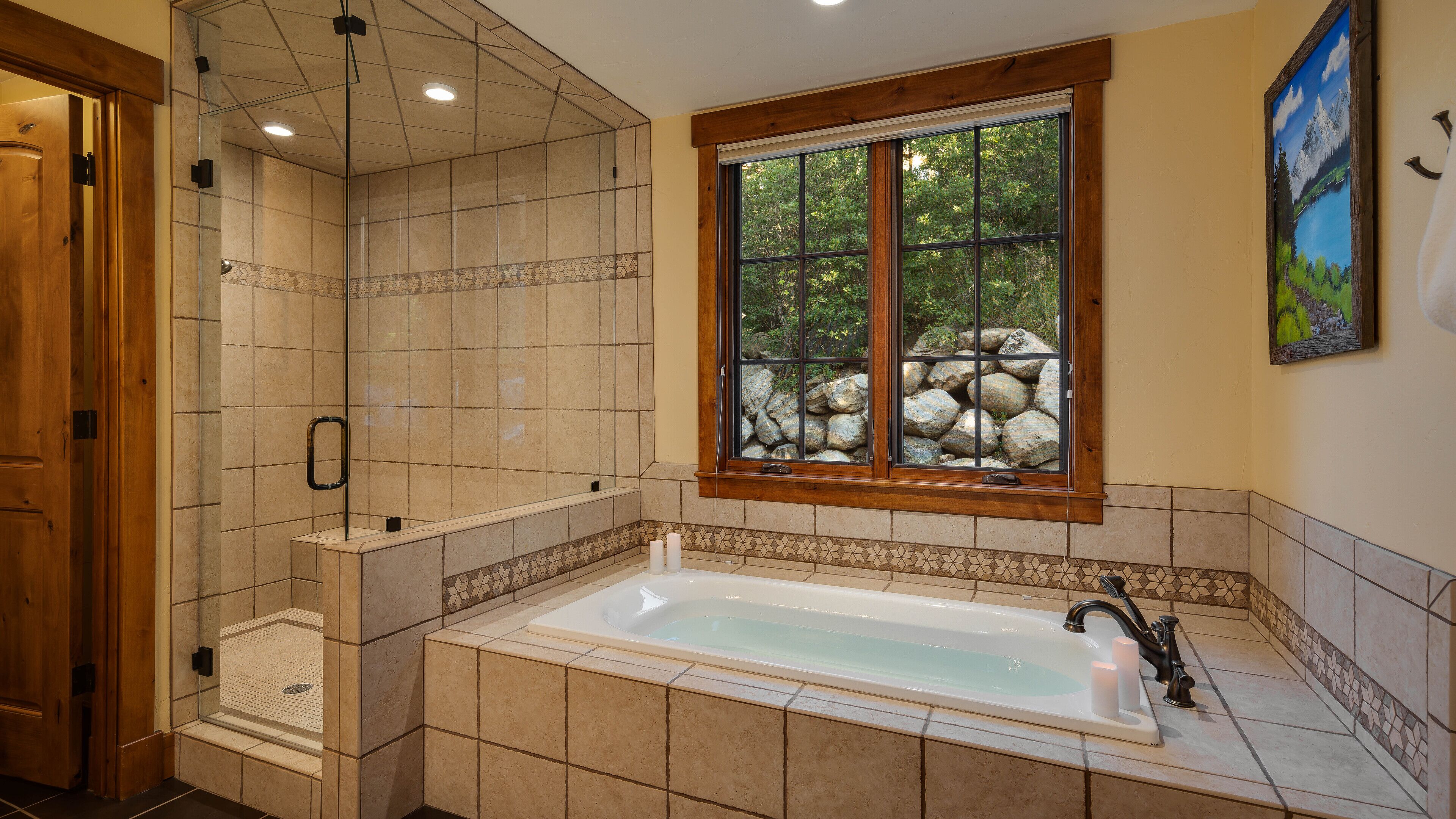 Un baño con bañera, ducha y ventana con vistas a rocas y vegetación.