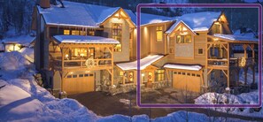 A large, multi-story chalet with a snow-covered roof and multiple balconies, surrounded by a snowy landscape.