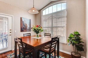 A dining area with a wooden table, chairs, a vase of flowers, and a painting on the wall.