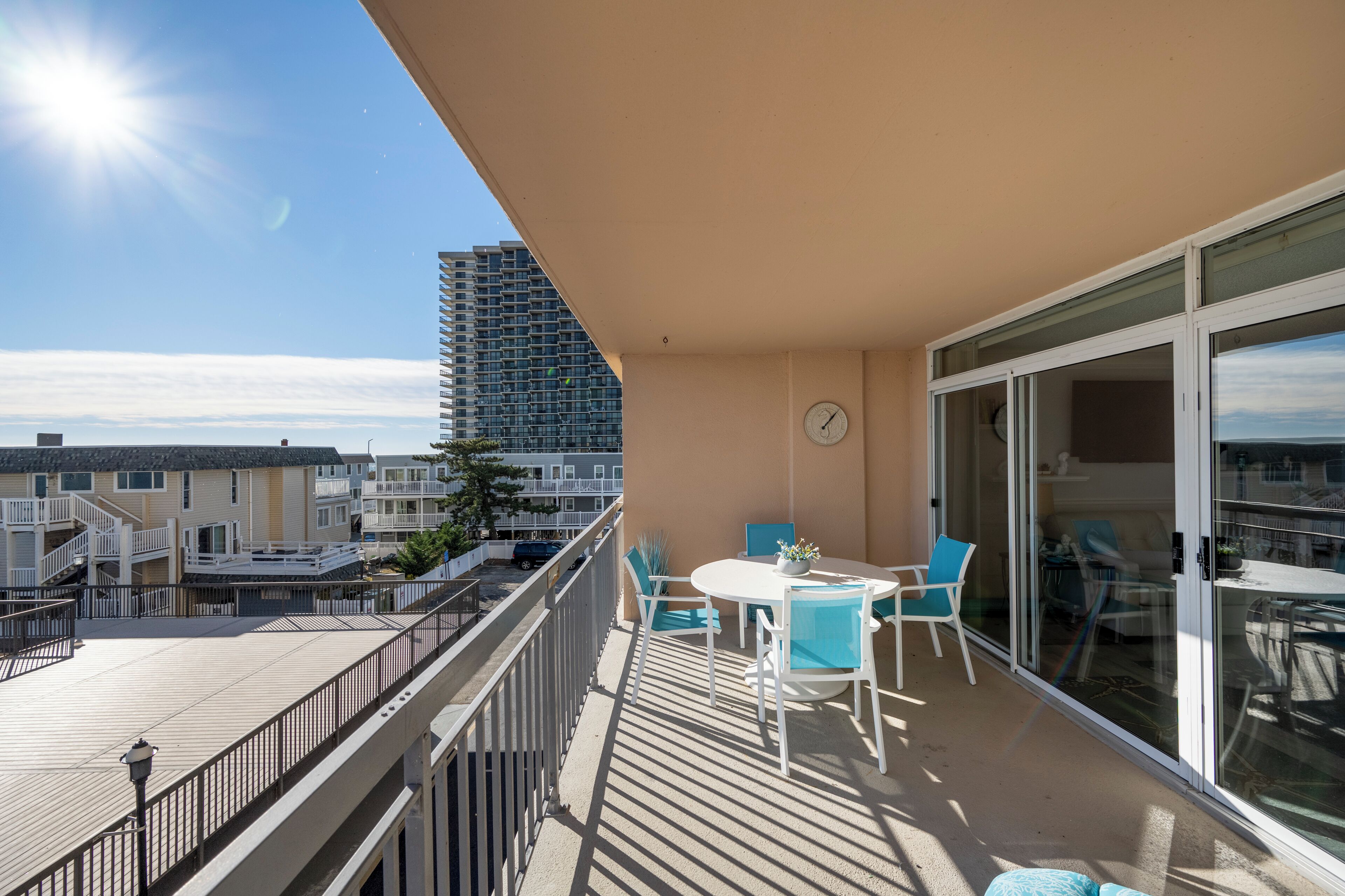 En balkon med et bord, stole, et ur og udsigt til en høj bygning.
