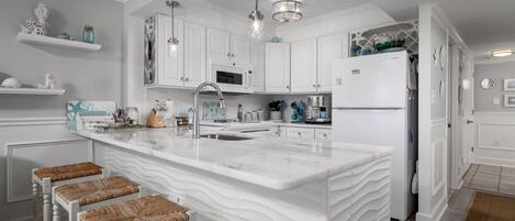 Une cuisine moderne avec des meubles blancs, un grand îlot central doté de tabourets, des appareils en acier inoxydable et des objets décoratifs disposés sur des étagères.