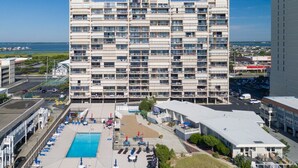 A multi-story hotel with a pool area, outdoor seating, and a view of the ocean. - Beautiful one bedroom oceanfront condo with stunning ocean views and a pool! (Ocean City)