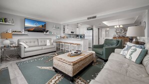 A modern living room with a sofa, armchair, and a coffee table. There is a kitchen area with cabinets and a refrigerator. - Beautiful one bedroom oceanfront condo with stunning ocean views and a pool! (Ocean City)
