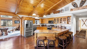 A spacious kitchen with wooden cabinets, a large island with stools, stainless steel appliances, and a high ceiling with exposed beams.