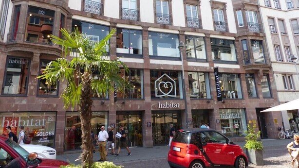 A multi-story building with 'habitat' store fronts, a palm tree, and a red car parked in front.