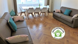 A living room with a sofa, a dining table with chairs, and a window with curtains.