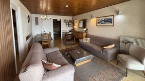 A cozy living room with a wooden ceiling, a sofa, a coffee table, and a dining area in the background. - Spacious 4-Room Apartment for 9 - Ski Lift, Balcony, Garage - Alpe d'Huez (Huez)