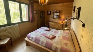 A cozy bedroom with a wooden bed, a bedside table, a dresser, and a window with curtains. - Spacious 4-Room Apartment for 9 - Ski Lift, Balcony, Garage - Alpe d'Huez (Huez)