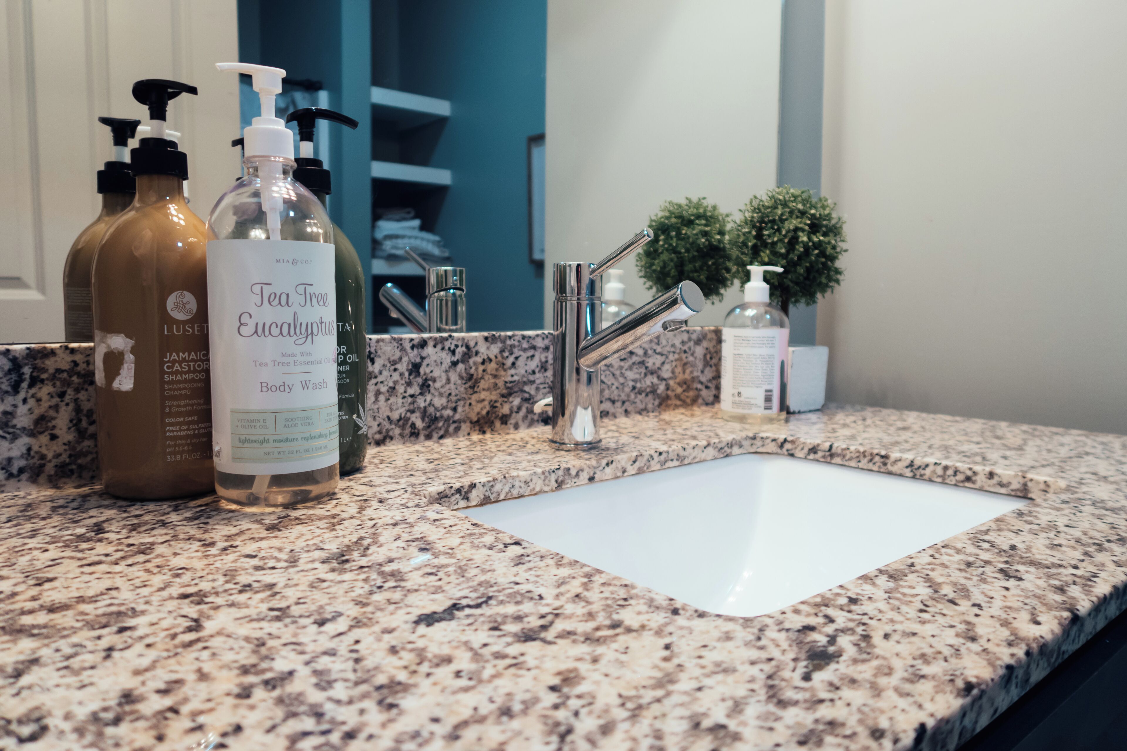 Une salle de bain dotée d’un comptoir en granit, d’un lavabo blanc et de divers produits de toilette, notamment un gel douche et un shampooing.