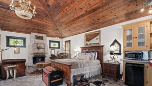 Ein rustikales Schlafzimmer mit Kamin aus Stein, Holzboden und einem Bett mit Streifenmuster.