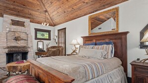Ein traditioneller Raum mit Holzbalkendecke, Kamin aus Stein, einem Bett mit gestreifter Bettdecke und einem großen Spiegel über dem Bett.
