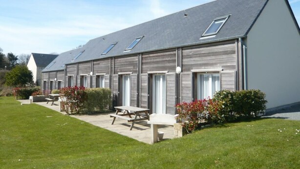 A row of single-story buildings with large windows and a sloped roof. - Cozy house in La Hague (La Hague)
