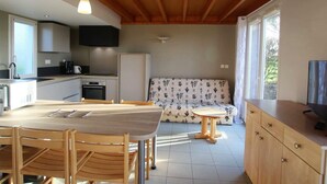 A modern kitchen with wooden beams, a dining table with chairs, a sofa, and a TV on a cabinet. - Cozy house in La Hague (La Hague)