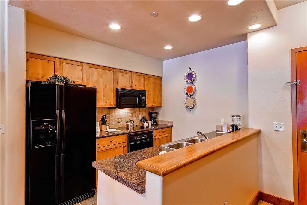A compact kitchen with wooden cabinets, a black refrigerator, a microwave, and a sink.