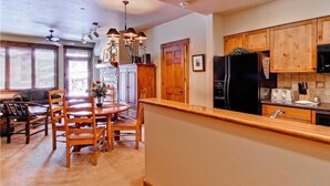 Una cocina con armarios de madera, un refrigerador negro y un comedor con sillas y mesa de madera.