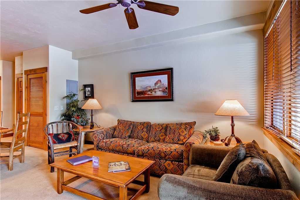 A living room with a sofa, armchairs, a coffee table, a ceiling fan, and a framed picture on the wall.