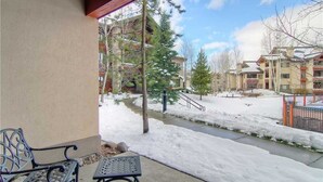 Un espacio al aire libre cubierto con un banco y una mesa, un sendero cubierto de nieve y edificios al fondo.