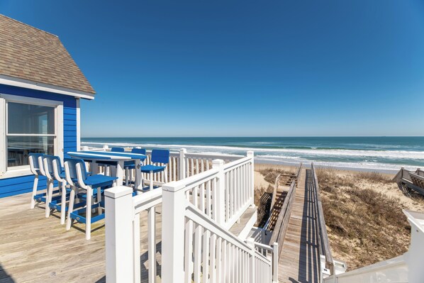 A wooden deck with blue chairs and tables, overlooking a beach.